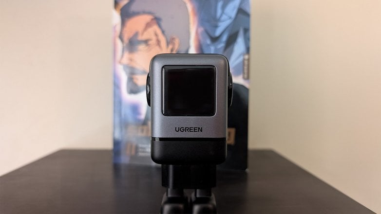 Chargeur Ugreen Uno 100W au design noir sur une table, avec un livre d'anime en arrière-plan.