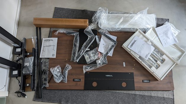 Zerlegte Vernal-Schreibtischkomponenten mit Anleitungen und Verpackung auf einem Bodenmatte.