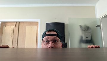 Eine Person, die überrascht über einen Tisch schaut, in einem Raum mit einer Glastür und einem Kleiderschrank.