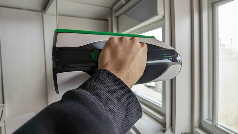 Eine Hand hält einen Vorwerk Kobold VG100 Plus Fensterreiniger in der Nähe eines Fensters.