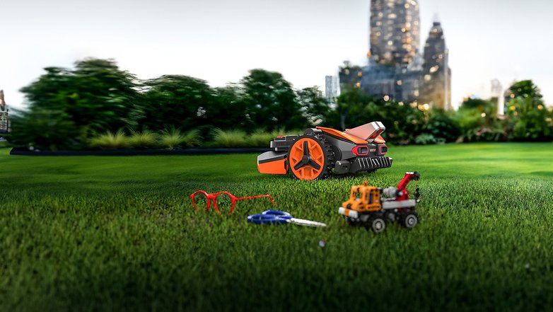 Ein Worx Landroid Rasenmäher auf Gras mit verstreutem Spielzeug und Brille. Ein Worx Landroid Rasenmäher auf Gras mit verstreutem Spielzeug und Brille.