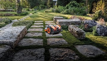 Ein Rasenmäher-Roboter, der auf Steinwegen in einem Landschaftsgarten fährt.