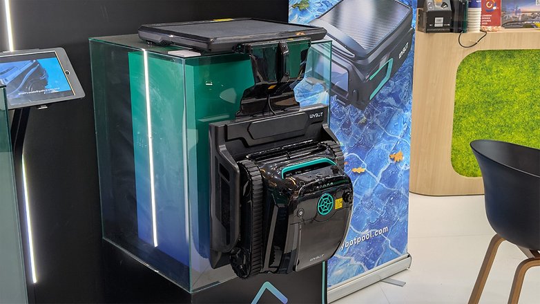 Ein robotischer Poolreiniger wird in einem Glaskasten mit einem Tablet daneben präsentiert. Ein robotischer Poolreiniger wird in einem Glaskasten mit einem Tablet daneben präsentiert.