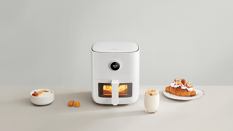 Ein Xiaomi Smart Air Fryer Pro auf einem Tisch mit Lebensmitteln, darunter Joghurt, Croissant und Früchte.