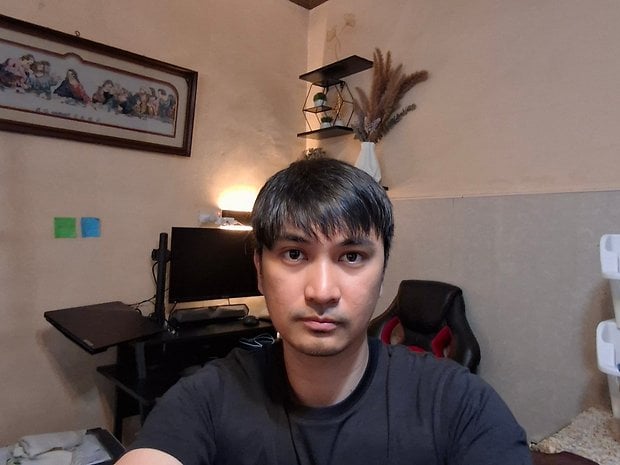 A person takes a selfie in a room with a computer desk and plants.
