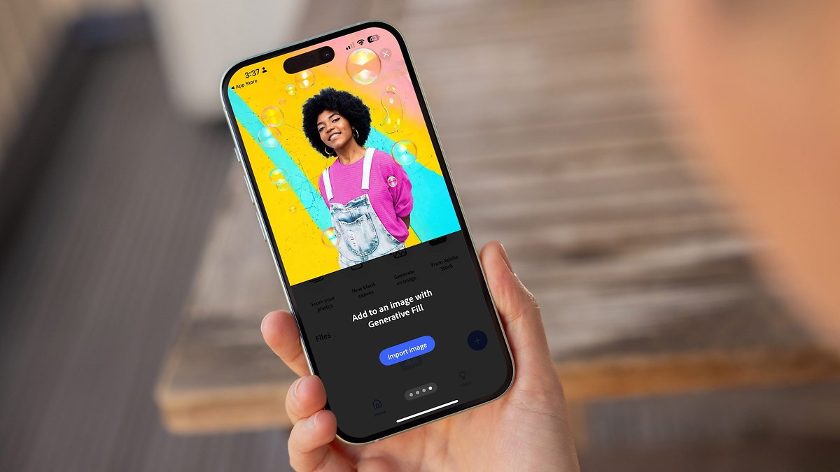 Une personne tient un smartphone affichant l'application Adobe Photoshop avec un design graphique coloré.