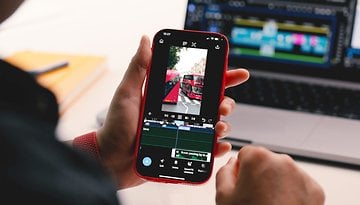 A person holding a smartphone displaying video editing software and a bus scene.