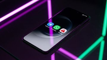 Un teléfono inteligente que muestra tres íconos de aplicaciones de mensajería: Telegram, WhatsApp y Signal sobre una superficie reflectante con luces de neón.