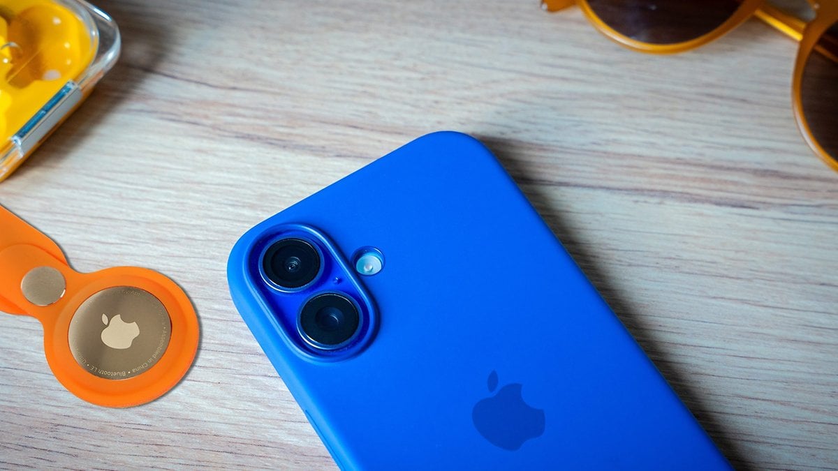 Un smartphone bleu à côté d'un AirTag Apple orange et d'écouteurs jaunes sur une surface en bois.