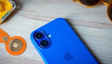 A blue smartphone beside an orange Apple AirTag and yellow earbuds on a wooden surface.