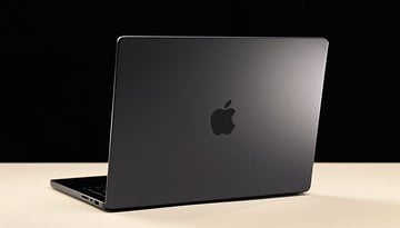 A black Apple MacBook Pro laptop viewed from the back on a light surface.