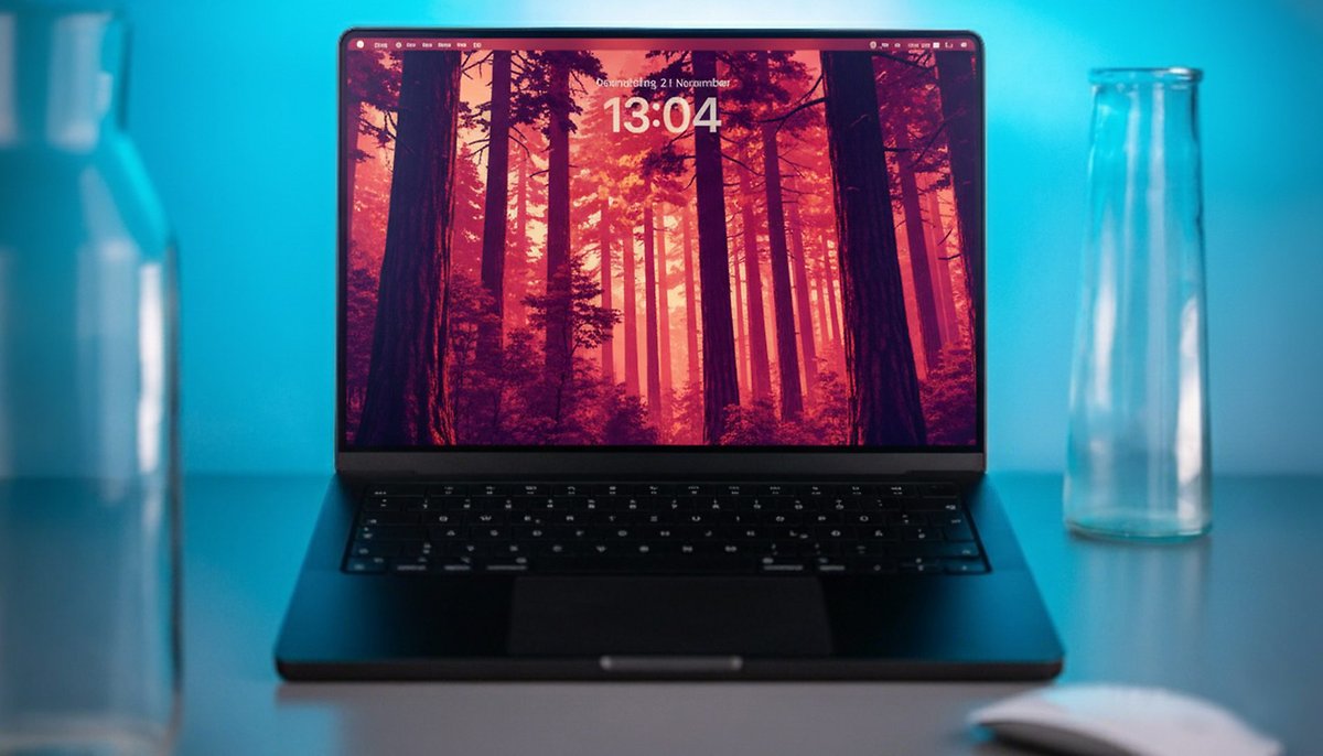Un MacBook Pro en un escritorio mostrando un fondo de bosque con la hora 13:04.