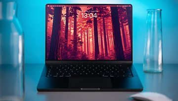 A MacBook Pro on a desk displaying a forest wallpaper with the time 13:04.