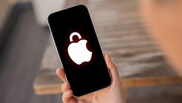 A hand holding an Apple iPhone 15 Pro displaying a locked Apple logo on the screen.