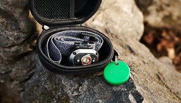 Eine schwarze Reißverschlusstasche auf einem Stein mit einer Stirnlampe und einem grünen Chipolo-Pop-Tracker.