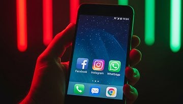 A hand holding a smartphone displaying Facebook, Instagram, WhatsApp, and other apps on the screen.
