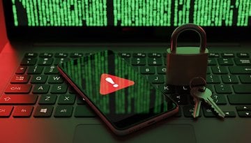 Um teclado de laptop com um smartphone exibindo um símbolo de aviso e um cadeado com chaves, contra um fundo de código verde.