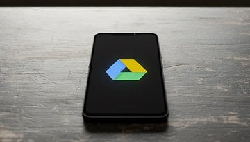 A smartphone displaying the Google Drive logo on a wooden surface.