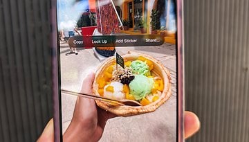 A hand holding a bowl of colorful ice cream with mango, green, and white flavors, displayed on a smartphone screen.