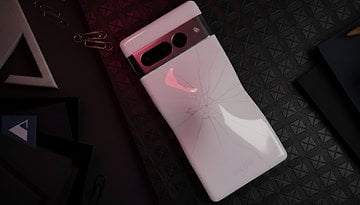 A Google Pixel 7 Pro smartphone with a cracked back, resting on a textured black surface with paper clips and stationery.
