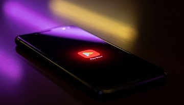 A smartphone displaying the Play Store app icon on a dark surface with colorful lighting.