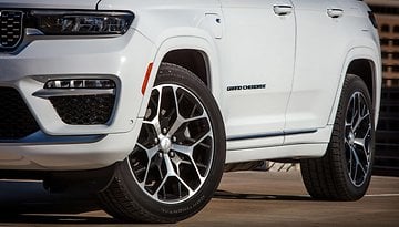 Close-up of a white Jeep Grand Cherokee L showing the front wheel and brand badge.