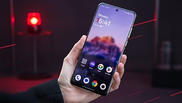 A hand holds a OnePlus 13 smartphone displaying the time 15:41 and a blurred scenic wallpaper.