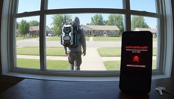 A person with a backpack is seen through a window, while a phone displays a critical alert message.