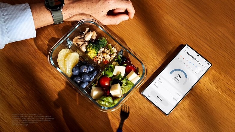 A hand rests next to a healthy meal and a Samsung phone displaying health metrics. A hand rests next to a healthy meal and a Samsung phone displaying health metrics.