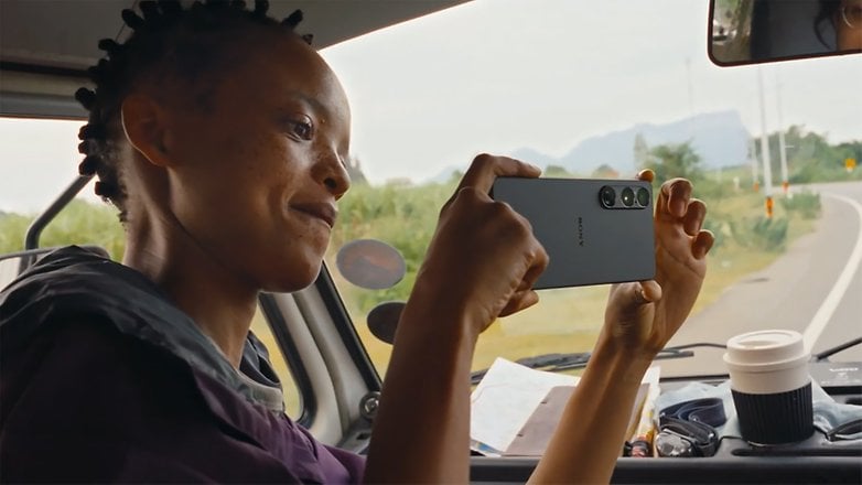 A person in a vehicle holding a Sony Xperia 1 VII smartphone, smiling while taking a photo. A person in a vehicle holding a Sony Xperia 1 VII smartphone, smiling while taking a photo.