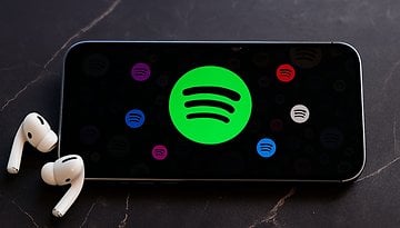 A smartphone displaying the Spotify logo with AirPods beside it.