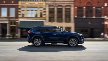 A blue Toyota RAV4 driving past historic buildings on a street.