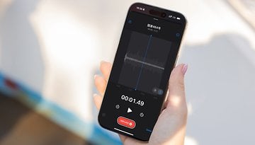 A hand holding an Apple iPhone 16 Pro displaying a voice recording screen with waveform and timer.