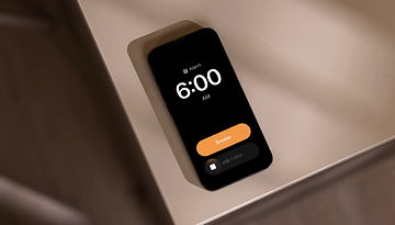 An Apple iPhone displaying an alarm set for 6:00 AM with a 'Snooze' button.