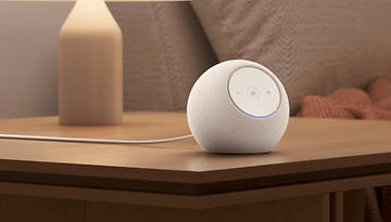 A white Amazon Echo Dot Max speaker on a wooden table next to a lamp.