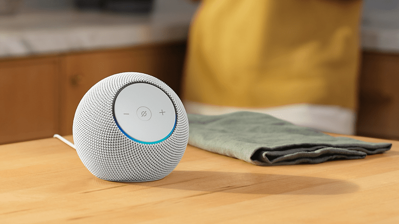 Ein weißer Amazon Echo Dot Max Lautsprecher auf einem Holztisch mit einem grünen Tuch in der Nähe.