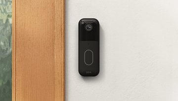 Eine Blink Video-Türklingel, die an einer Wand neben einem Holzrahmen montiert ist.