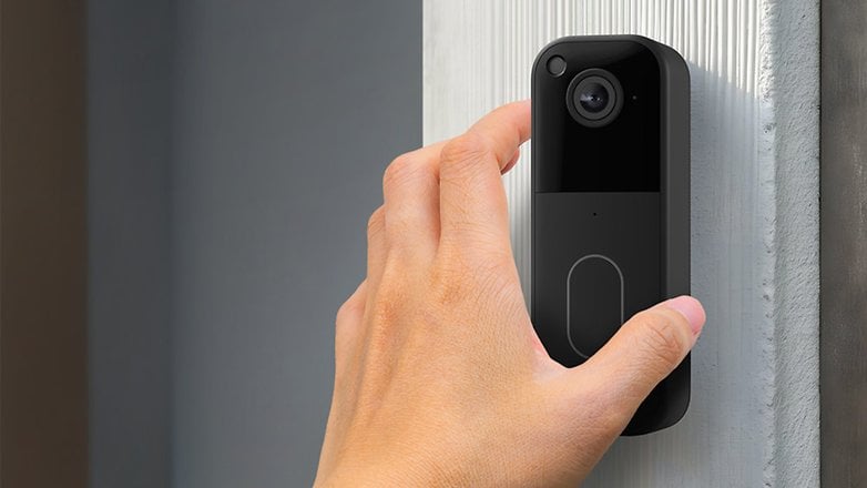 Eine Person drückt einen Knopf an einer schwarzen Video-Türklingel, die an einer Wand montiert ist. Eine Person drückt einen Knopf an einer schwarzen Video-Türklingel, die an einer Wand montiert ist.