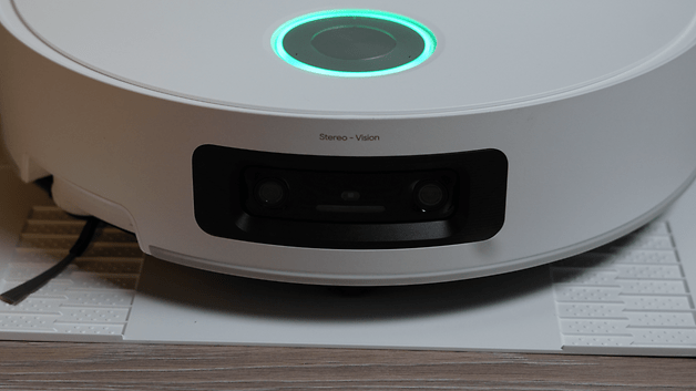 Weißer Staubsaugerroboter mit grünem Licht und Stereo-Visionskameras auf einer strukturierten Oberfläche.