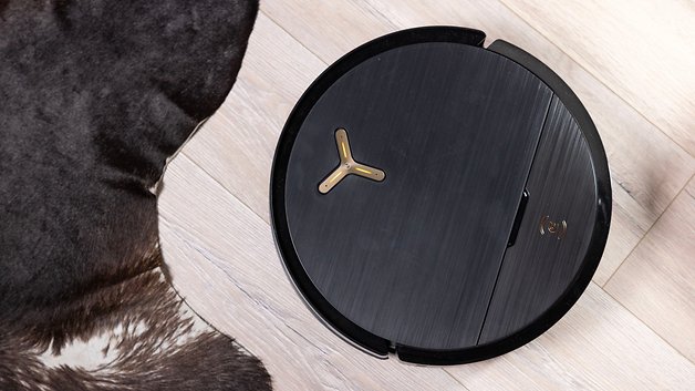 Ein schwarzer Ecovacs Deebot X9 Pro Omni Staubsauger auf Holzboden neben einem braunen Pelzteppich.