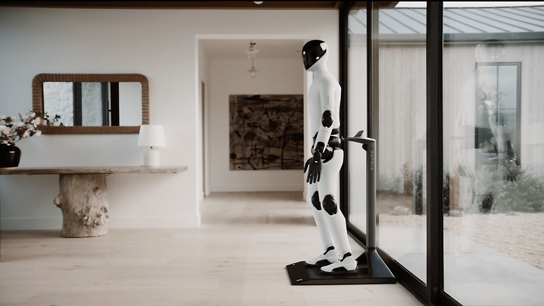 Ein humanoider Roboter steht in einem modernen Innenraum neben einem Tisch und einem großen Fenster.