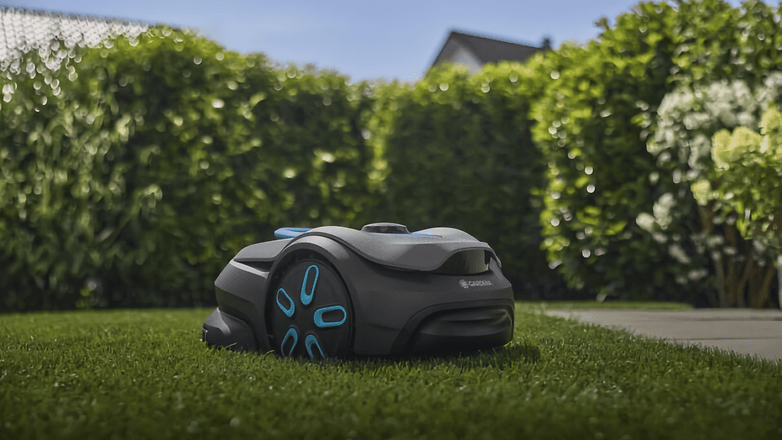 Ein Gardena Smart Sileno Sense Rasenmäher auf grünem Gras neben Hecken. Ein Gardena Smart Sileno Sense Rasenmäher auf grünem Gras neben Hecken.