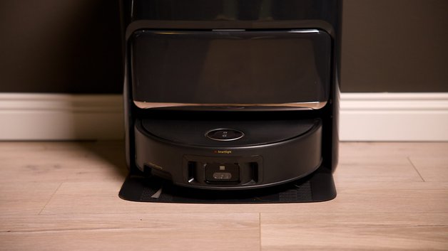 Ein Mova Z60 Ultra Roller Complete Roboterstaubsauger, der auf einer Dockingstation gegen eine dunkle Wand auflädt.