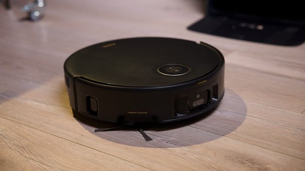Ein schwarzer Staubsauger-Roboter steht auf einem Holzboden.