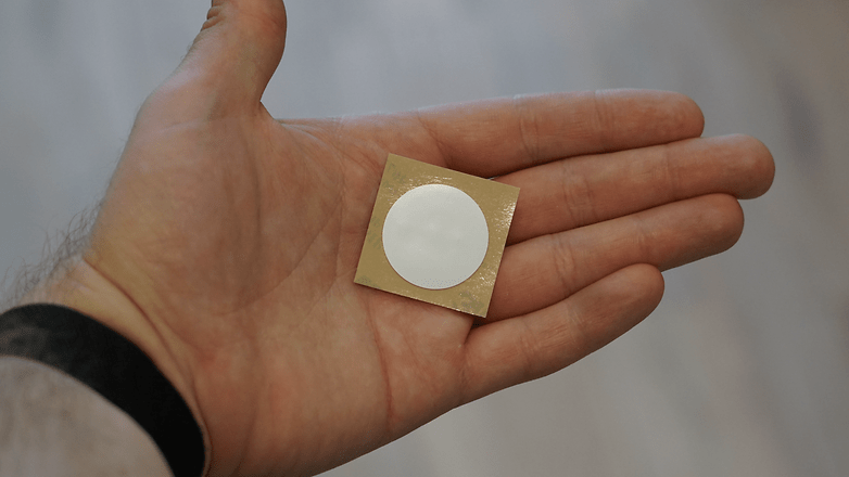 Eine Hand hält einen runden NFC-Aufkleber auf goldenem Hintergrund. Eine Hand hält einen runden NFC-Aufkleber auf goldenem Hintergrund.