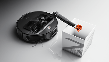 Roborock Saros Z70 robot vacuum with a robotic arm depositing an object into a white container.