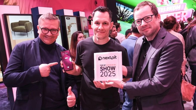 Drei Männer auf einer Technologiemesse halten ein Smartphone und ein Schild mit der Aufschrift 'nextpit Top of Show 2025'.