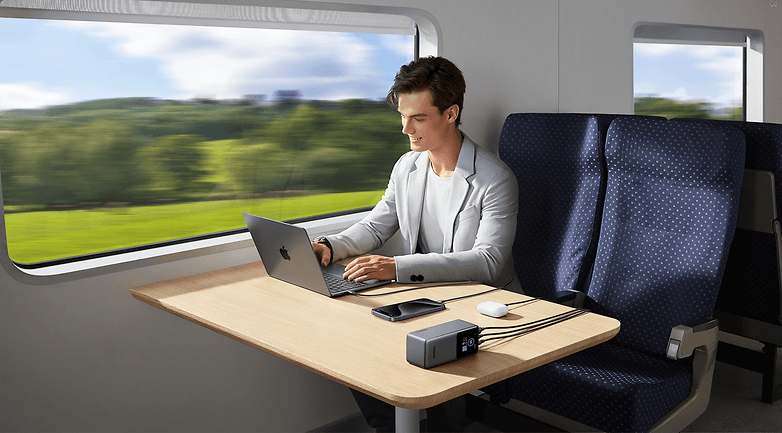 Un home rechargeant son pc portable avec une batterie externe Ugreen dans un train.