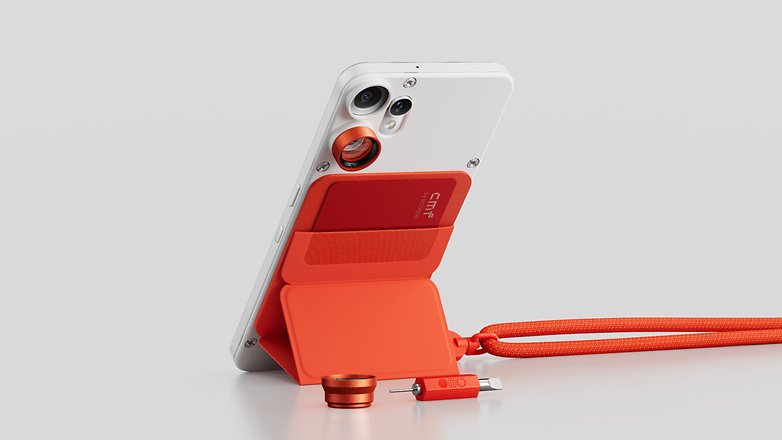 Nada CMF Phone 2 Pro em branco com acessórios vermelhos, incluindo um suporte e um cabo de carregamento. Nada CMF Phone 2 Pro em branco com acessórios vermelhos, incluindo um suporte e um cabo de carregamento.