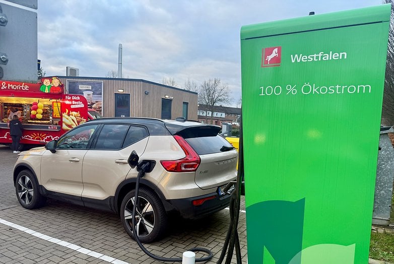 Une voiture électrique Volvo EX40 se charge à une station avec un panneau vert indiquant '100 % Ökostrom'.